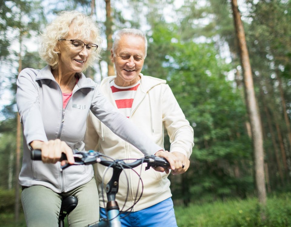 Senior man teaching his wife how to ride bicycle while chilling in park on summer day