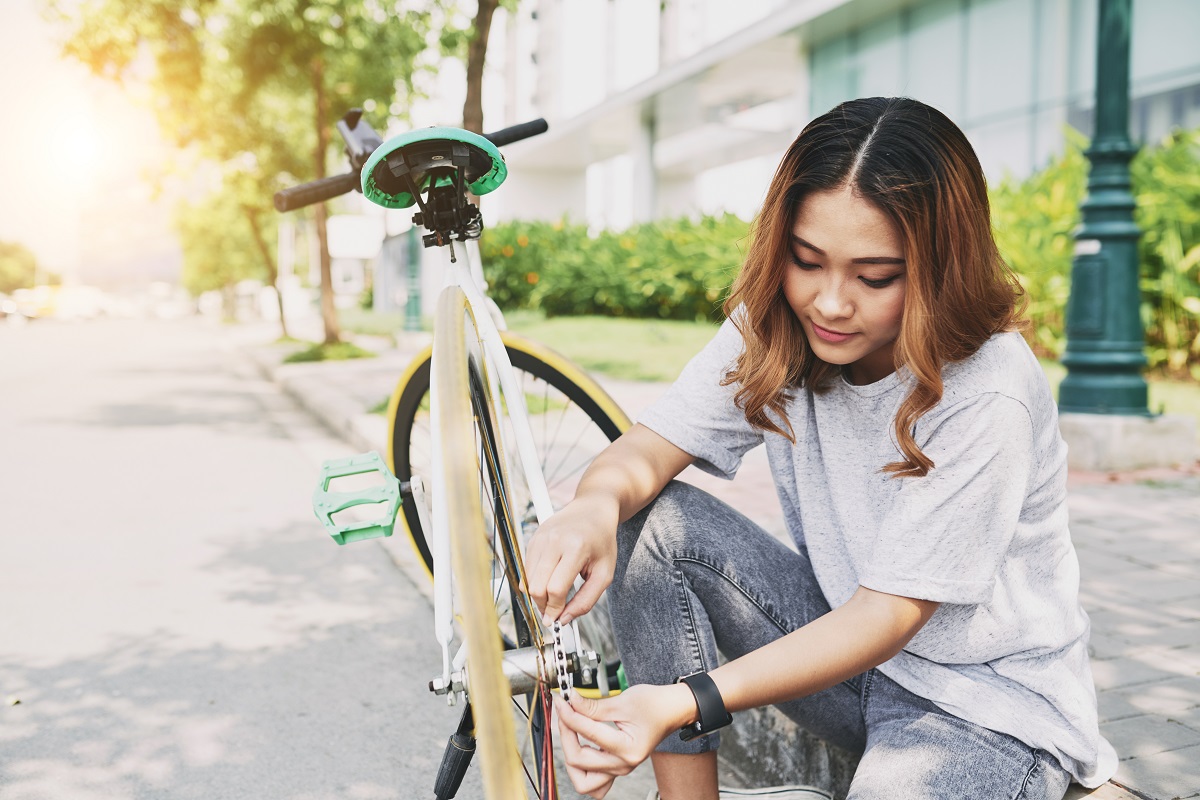 Pretty young Vietnamese woman fixing her bicycle after long ride